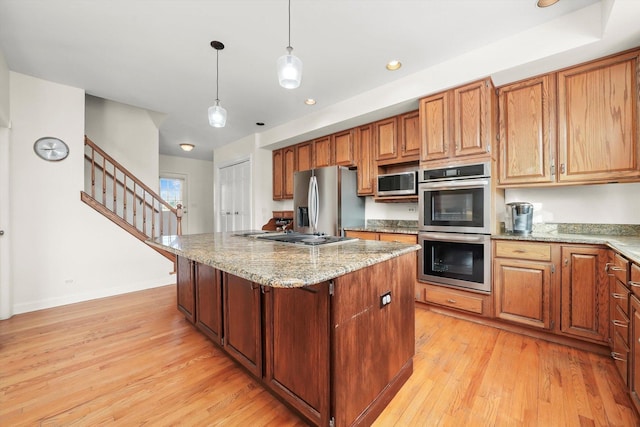 kitchen featuring stainless steel appliances, a kitchen island, light wood-type flooring, light stone counters, and hanging light fixtures