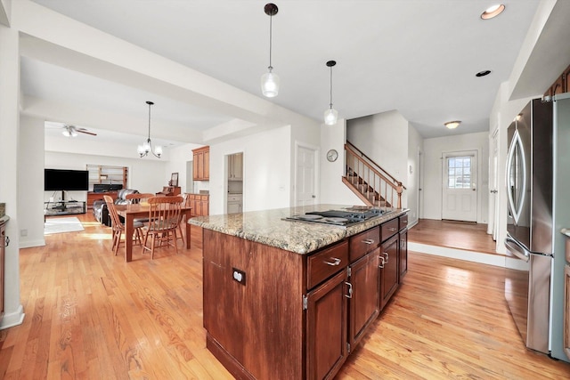 kitchen featuring gas cooktop, a kitchen island, light stone counters, light wood-style floors, and freestanding refrigerator