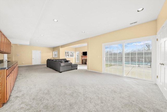 living room featuring light carpet, visible vents, plenty of natural light, and a fireplace with raised hearth