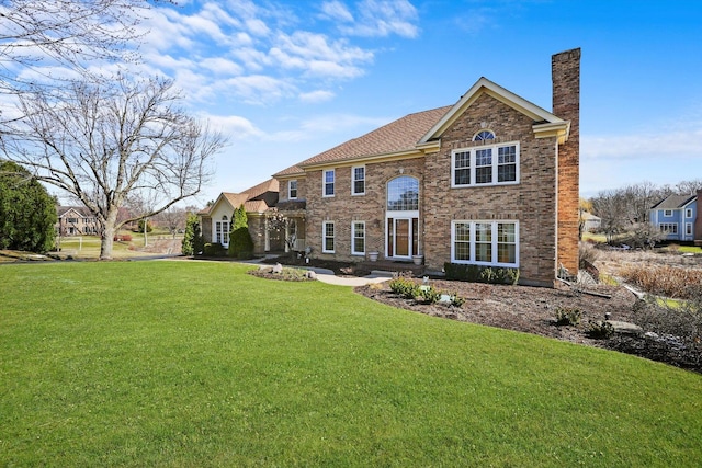rear view of property featuring a chimney, brick siding, and a yard