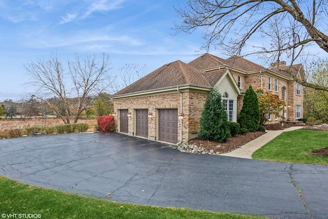 view of side of property with driveway, roof with shingles, a chimney, brick siding, and a garage