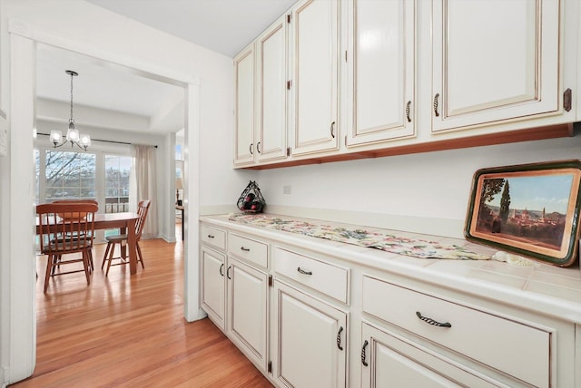 kitchen featuring light countertops, a chandelier, white cabinetry, hanging light fixtures, and light wood-type flooring