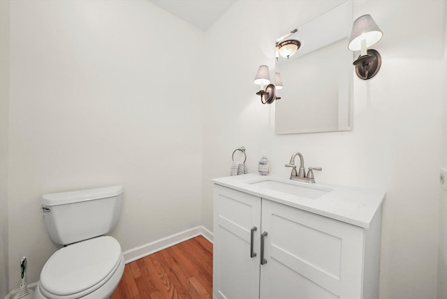 half bath with toilet, vanity, baseboards, and wood finished floors