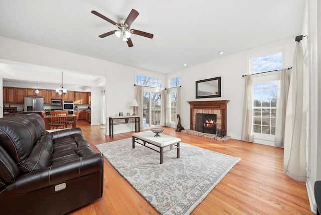 living room with light wood-style flooring, a brick fireplace, and ceiling fan