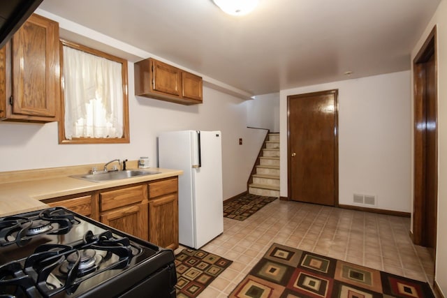 kitchen featuring light countertops, black gas range oven, a sink, freestanding refrigerator, and visible vents