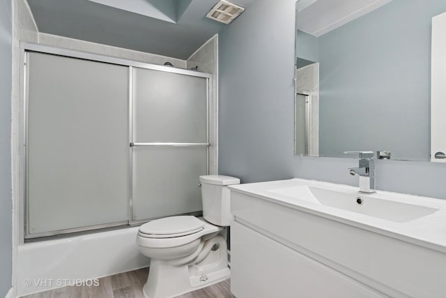 full bath with visible vents, vanity, wood finished floors, toilet, and bath / shower combo with glass door