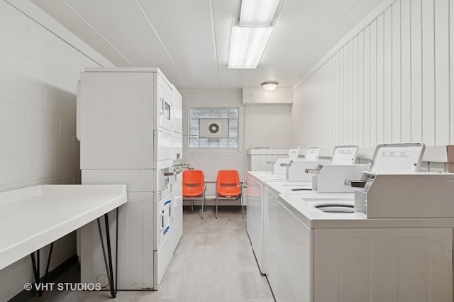community laundry room with concrete block wall, light wood-style floors, stacked washer / drying machine, and washer and clothes dryer