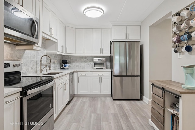 kitchen with light wood-type flooring, white cabinets, a sink, appliances with stainless steel finishes, and backsplash