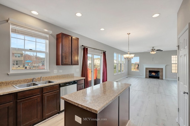 kitchen with a sink, stainless steel dishwasher, a ceiling fan, light countertops, and a tile fireplace