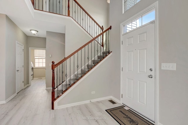 entrance foyer featuring wood finished floors, stairway, a high ceiling, baseboards, and washer / clothes dryer