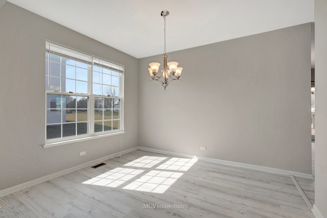unfurnished room with a chandelier, baseboards, and wood finished floors