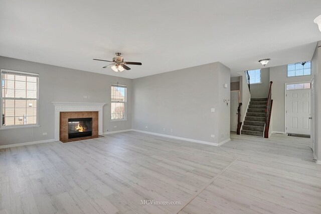 unfurnished living room with light wood-style flooring, baseboards, ceiling fan, stairs, and a tile fireplace