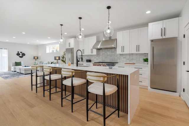 1522 W Wolfram St, Chicago, IL 60657 - kitchen with wall chimney range hood, appliances with stainless steel finishes, a center island with sink, a sink, and white cabinets