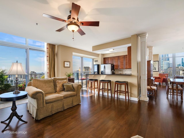 living area with ornate columns, a wall of windows, dark wood-type flooring, baseboards, and ceiling fan