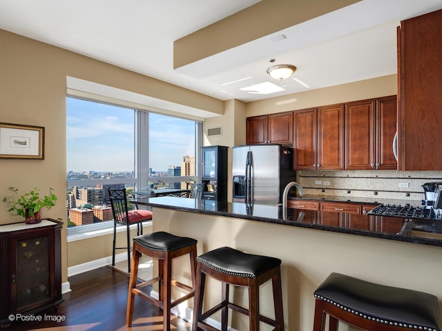 kitchen with dark stone counters, tasteful backsplash, a sink, stainless steel fridge with ice dispenser, and a breakfast bar area