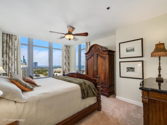 bedroom featuring baseboards, floor to ceiling windows, a ceiling fan, a view of city, and light colored carpet