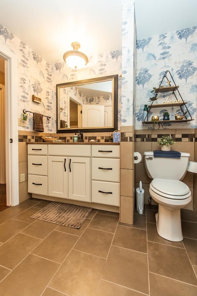 bathroom with wallpapered walls, toilet, tile patterned flooring, and wainscoting