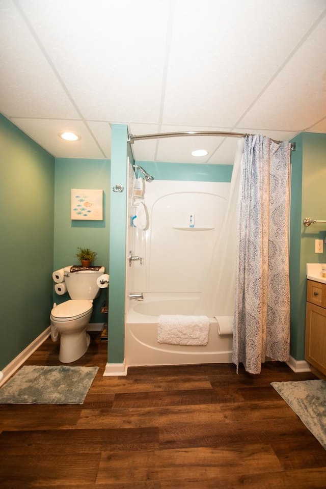 full bathroom featuring wood finished floors, toilet, shower / bathtub combination with curtain, and a paneled ceiling