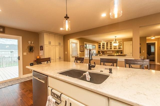 kitchen with light stone counters, a sink, stainless steel dishwasher, hanging light fixtures, and dark wood-style flooring