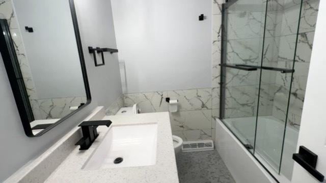 full bathroom with combined bath / shower with glass door, toilet, vanity, and tile walls