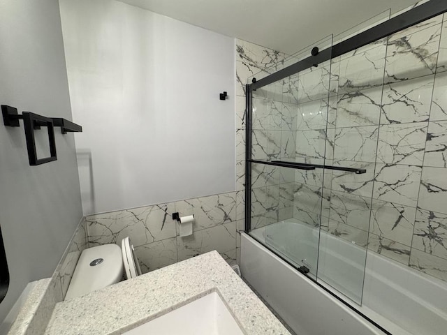 full bath with wainscoting, bath / shower combo with glass door, toilet, and tile walls