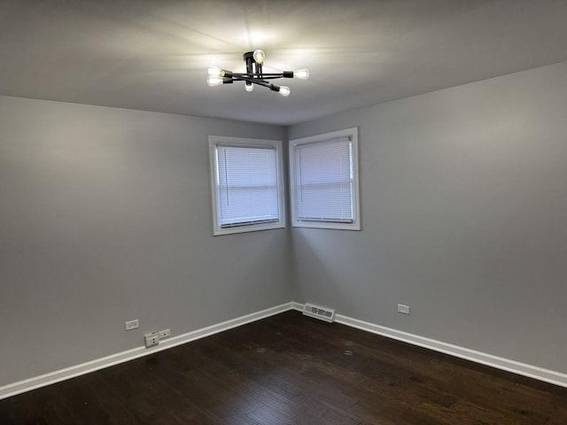 empty room featuring dark wood-style flooring, baseboards, a chandelier, and visible vents