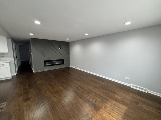 unfurnished living room featuring baseboards, dark wood-style flooring, visible vents, and a glass covered fireplace