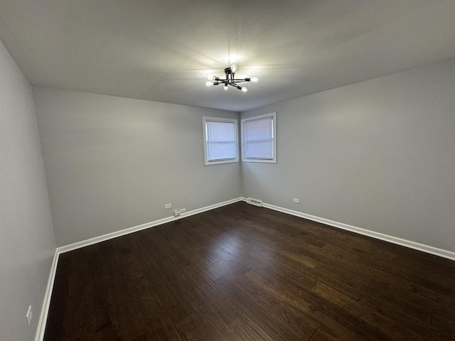 empty room with baseboards, dark wood-style flooring, visible vents, and a chandelier