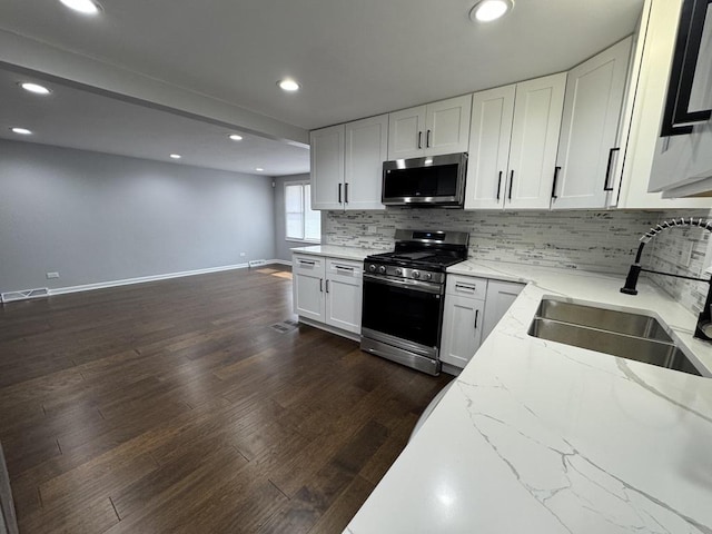 kitchen with a sink, tasteful backsplash, light stone countertops, appliances with stainless steel finishes, and dark wood-style flooring