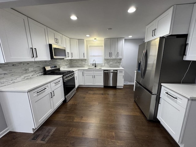 kitchen with dark wood-style flooring, appliances with stainless steel finishes, white cabinetry, a sink, and backsplash