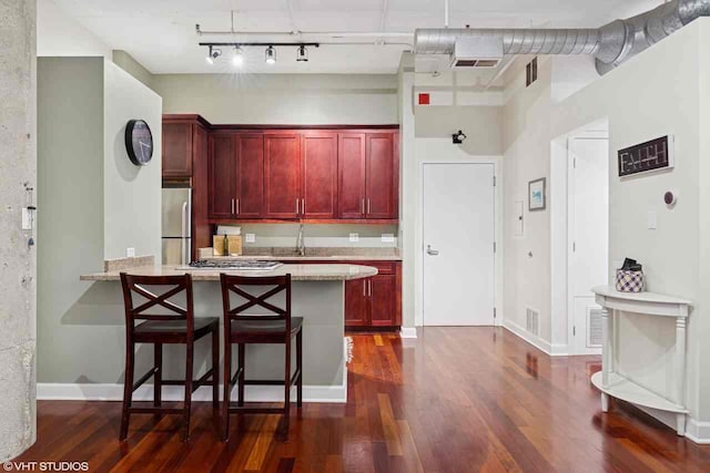 kitchen featuring stainless steel fridge, a kitchen breakfast bar, dark wood-type flooring, and dark brown cabinets