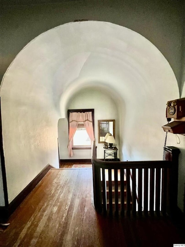 stairway with hardwood / wood-style floors, lofted ceiling, arched walkways, and baseboards