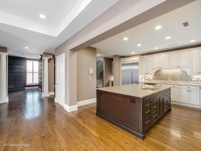 kitchen featuring white cabinets, light countertops, decorative columns, tasteful backsplash, and a sink