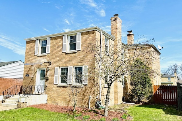 view of front of home featuring a chimney, brick siding, fence, and a front yard