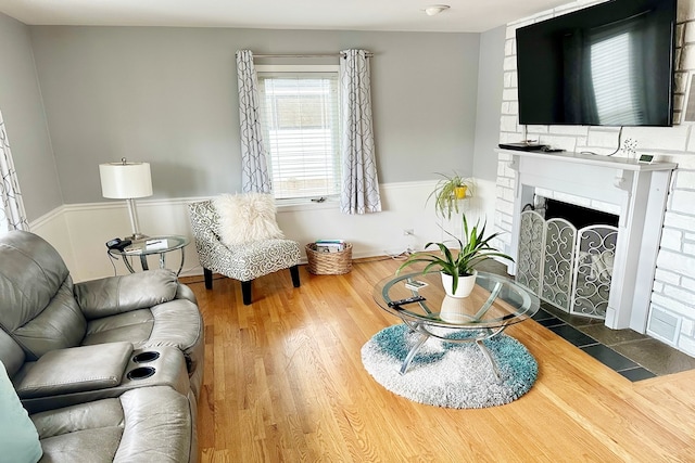 living area with wood finished floors, a wainscoted wall, and a fireplace with flush hearth
