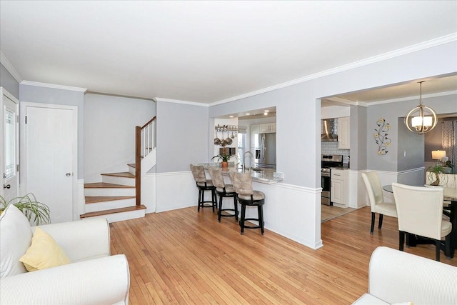 living room featuring light wood-type flooring, ornamental molding, and stairs