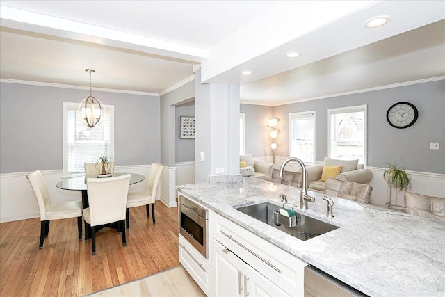 kitchen with white cabinets, light wood-style flooring, a sink, stainless steel appliances, and light stone countertops