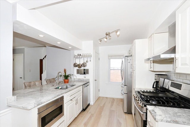 kitchen featuring a peninsula, a sink, appliances with stainless steel finishes, and white cabinetry
