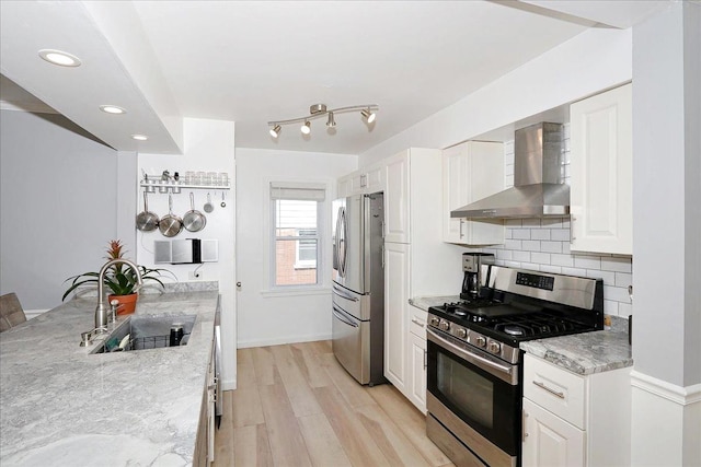 kitchen featuring wall chimney range hood, decorative backsplash, a sink, appliances with stainless steel finishes, and light wood-style floors