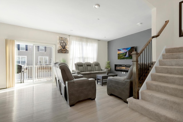 living room featuring a glass covered fireplace, stairway, and light wood-type flooring