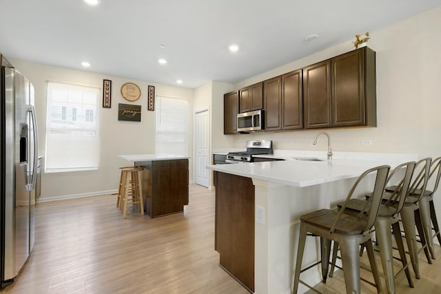 kitchen with light wood-type flooring, stainless steel appliances, a breakfast bar, a sink, and dark brown cabinets
