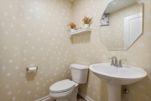 half bathroom with baseboards, toilet, and wallpapered walls