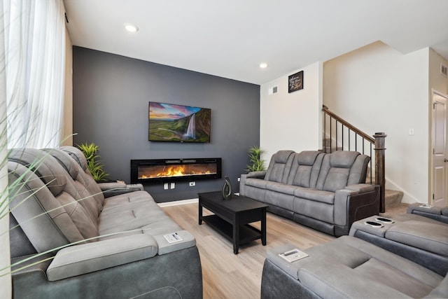 living room with stairs, recessed lighting, light wood-type flooring, visible vents, and a glass covered fireplace