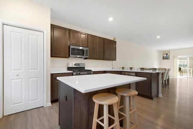 kitchen featuring a kitchen breakfast bar, light countertops, a peninsula, dark brown cabinets, and appliances with stainless steel finishes