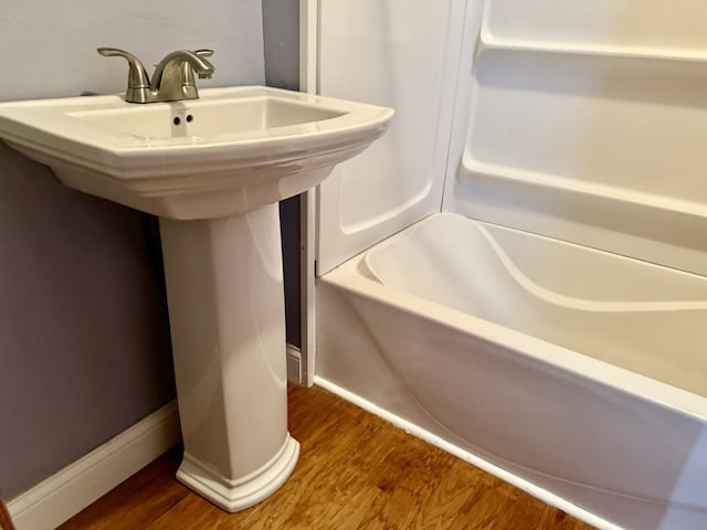 bathroom featuring baseboards, wood finished floors, a washtub, and a sink