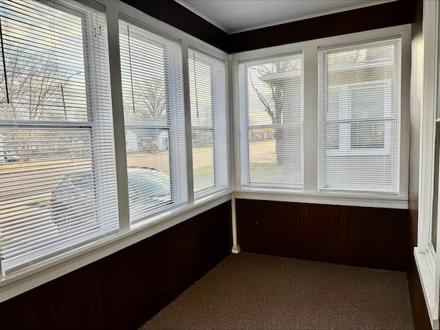 unfurnished sunroom featuring carpet floors, crown molding, and wooden walls