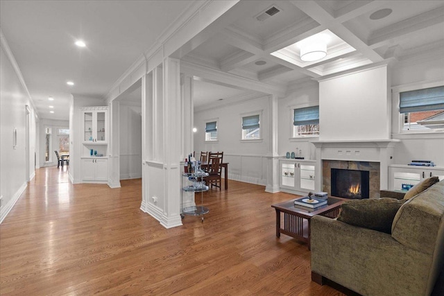 living area with light wood-style flooring, a tile fireplace, beamed ceiling, ornamental molding, and coffered ceiling