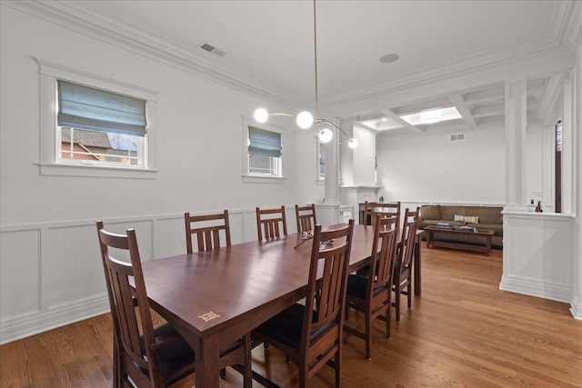 dining room with coffered ceiling, wood finished floors, a decorative wall, visible vents, and ornamental molding