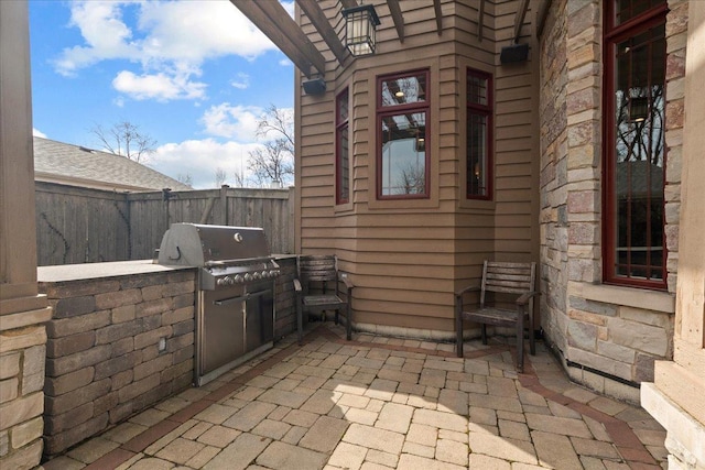 view of patio with exterior kitchen, fence, and a grill