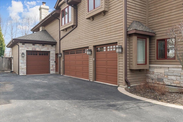 view of side of property featuring stone siding, a chimney, aphalt driveway, and an attached garage